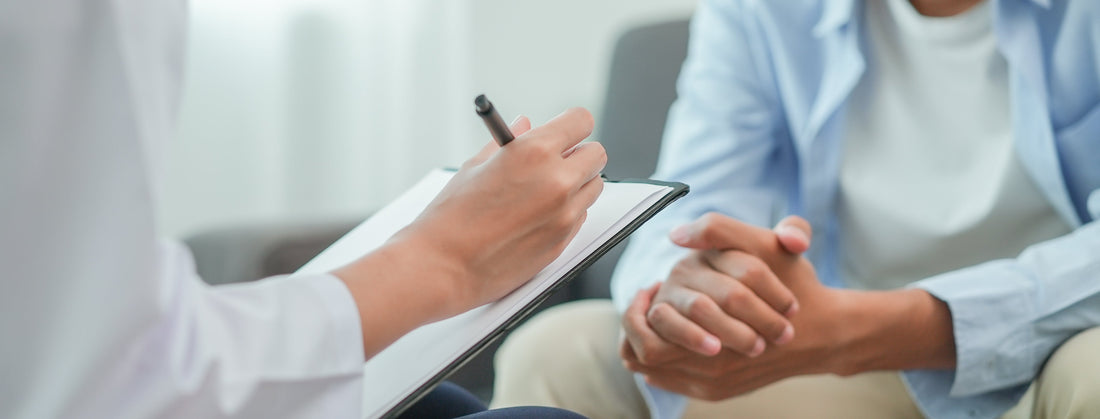 A wellness practioner taking notes while holding a patient's hand in a comforting manner during a consultation.
