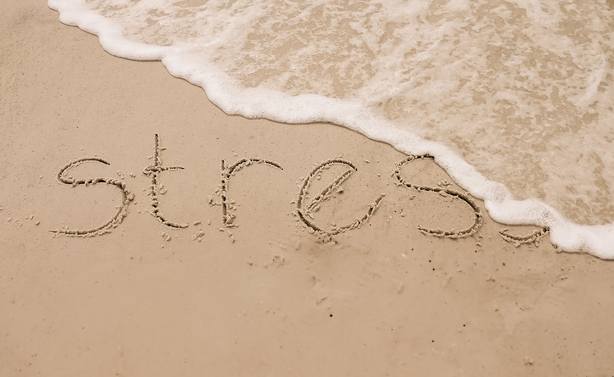 stress written in sand on a beach