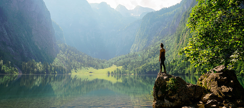 woman standing on rock overlooking lake in mountain valley
