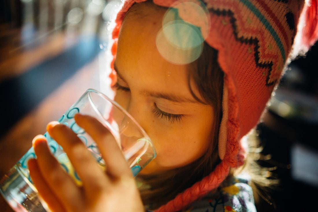 young child with orange hat drinking out of glass